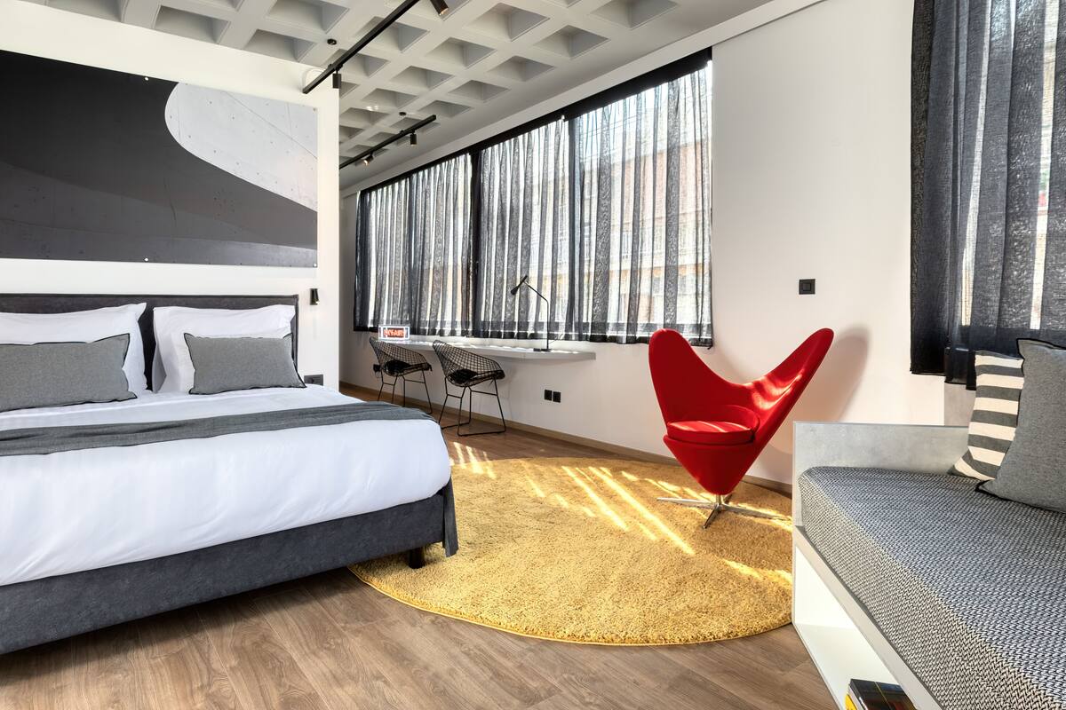A modern bedroom with a large bed, a red chair, and a sofa.