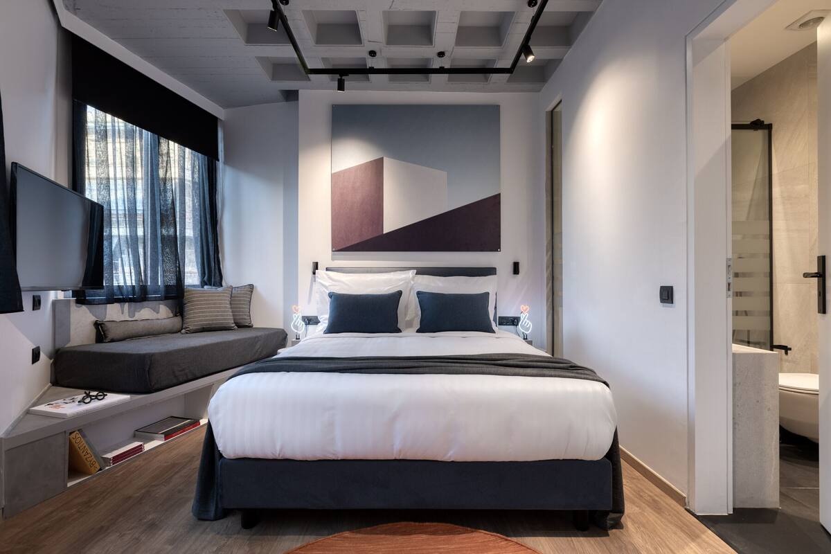 A modern bedroom with a large bed, bedside tables, a built-in bench, a TV, and a view of the outdoors.
