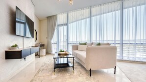 Ein modernes Wohnzimmer mit Fernseher, einer Couch, einem Couchtisch und einem großen Fenster mit durchscheinenden Vorhängen.