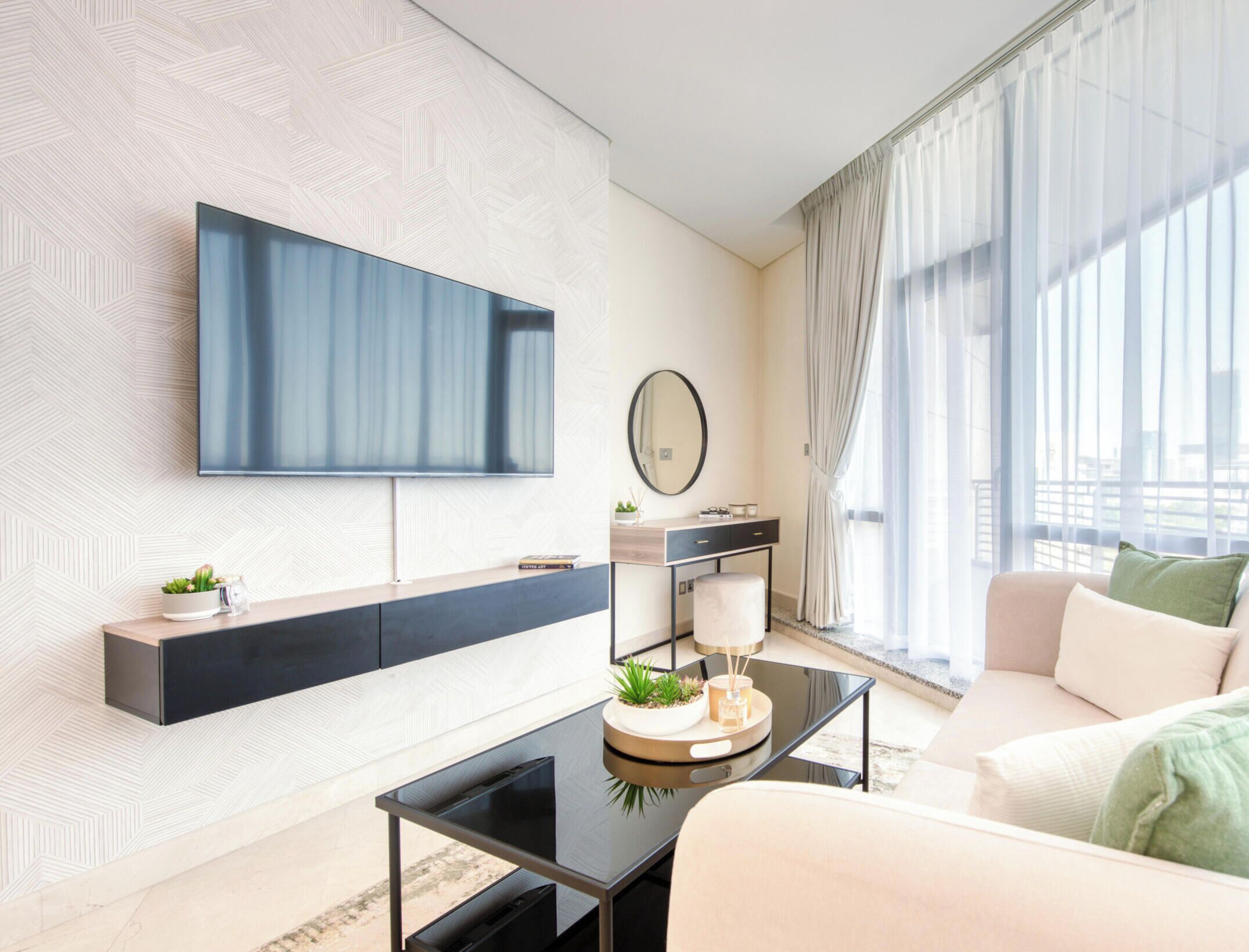 Een moderne woonkamer met een flatscreen televisie, een console tafel met decoratieve objecten, een bank en een groot raam met gordijnen.