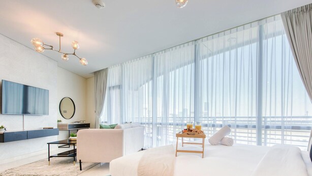Ein modernes Hotelzimmer mit einem großen Bett, einem Schreibtisch, einem Fernseher und Blick auf die Stadt durch leichte Vorhänge.