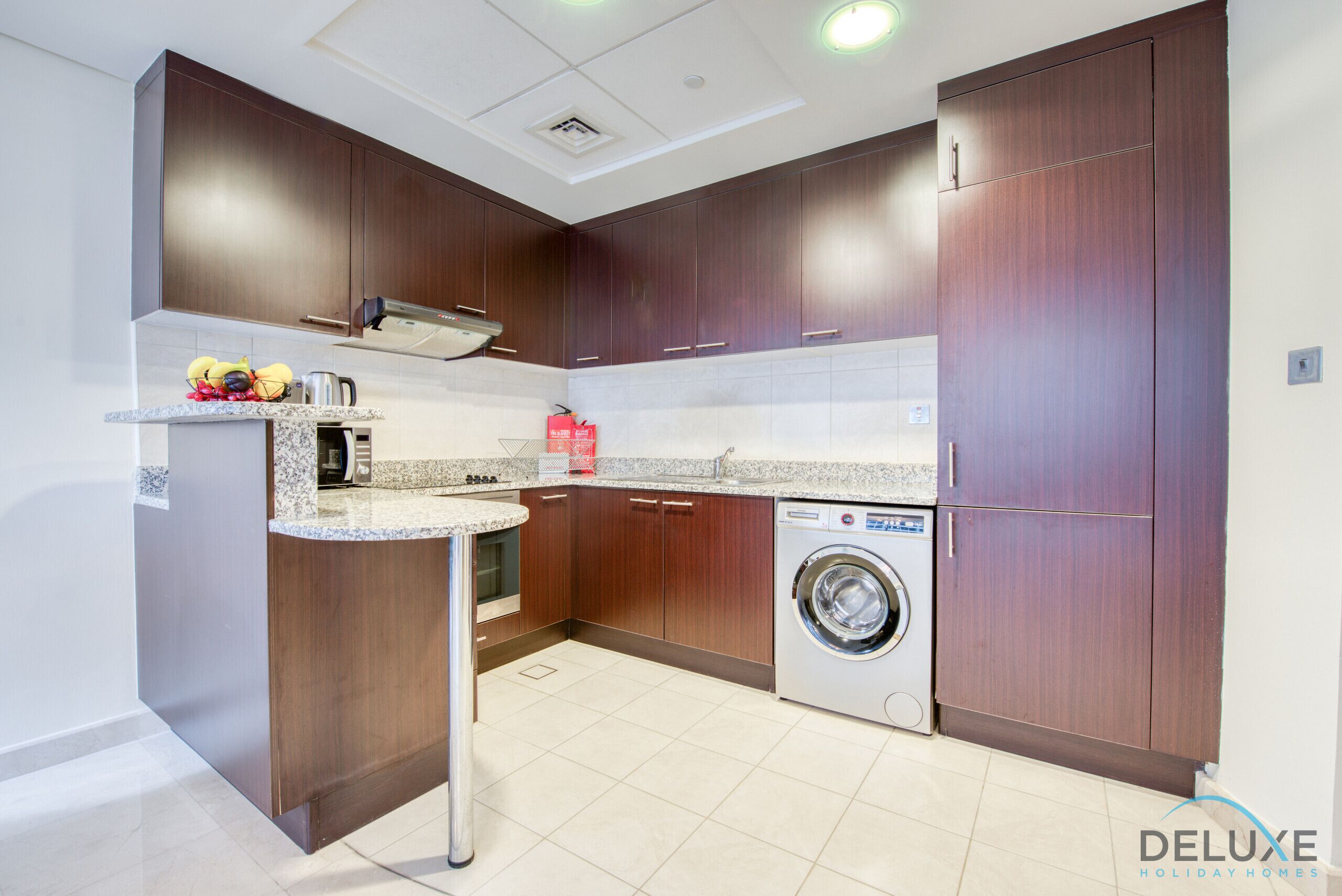 Une cuisine moderne avec des meubles de couleur bois foncé, un lave-linge encastré et un plan de travail en granit.