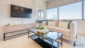 Ein modernes Wohnzimmer mit einer Couch, einem Couchtisch, einem an der Wand montierten Fernseher und einem großen Fenster mit Blick auf die Stadt.