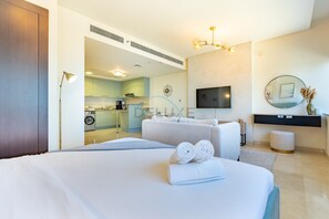 Habitación de hotel moderna con cama, sofá, televisión y una kitchenette al fondo.