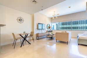 A modern living room with a dining area, a sofa, a coffee table, and a TV mounted on the wall. - Fresh Studio at Sky Gardens DIFC by Deluxe Holiday Homes (Dubai)