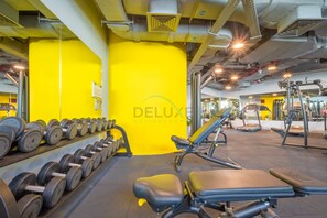 A gym with yellow walls, weightlifting equipment, and exercise machines. - Fresh Studio at Sky Gardens DIFC by Deluxe Holiday Homes (Dubai)
