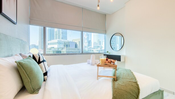 Una habitación de hotel con una cama grande, vista a la ciudad, un espejo redondo y una bandeja de desayuno.