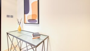 Un interior moderno con una mesa de vidrio, un florero con ramas y una obra de arte abstracta enmarcada en la pared.