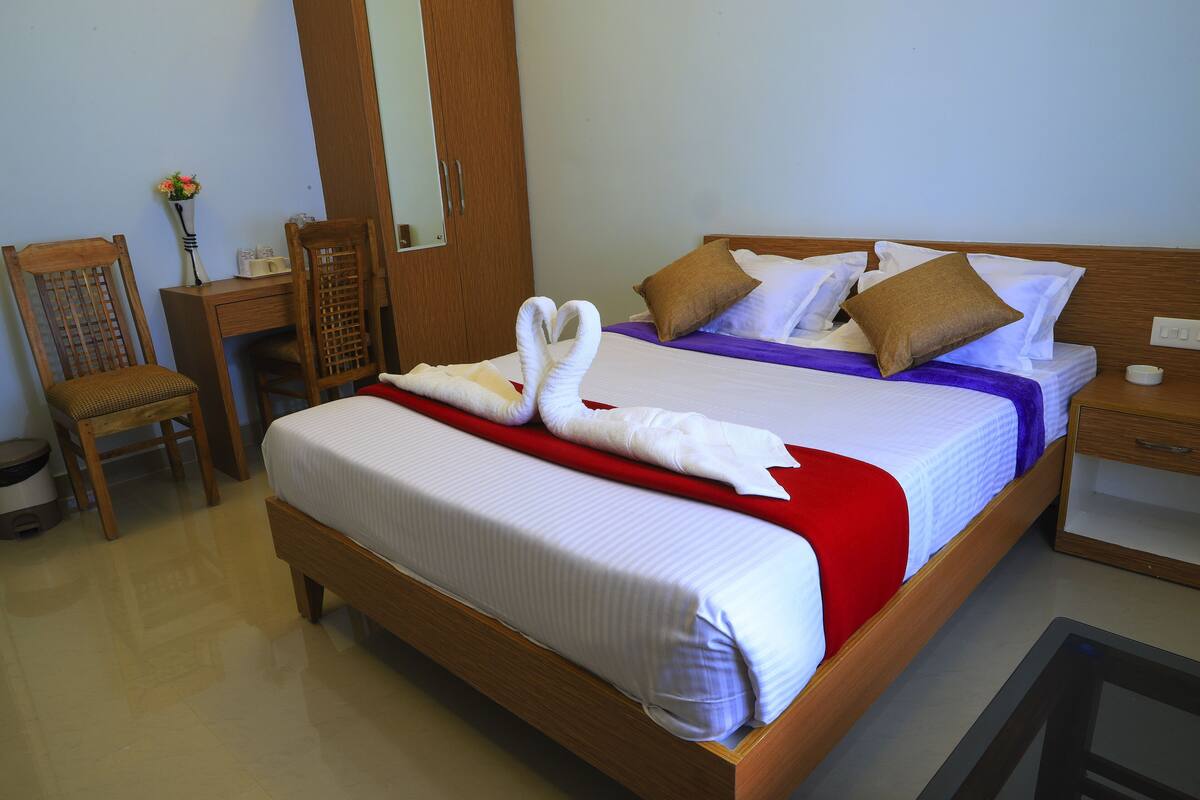 A neatly made bed with white linens, a red throw blanket, and two towels shaped like swans.