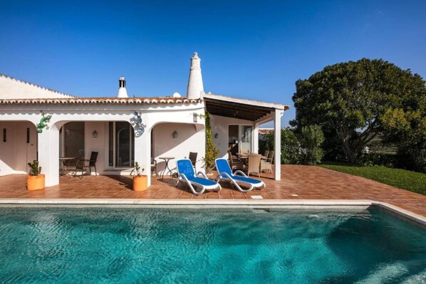 A house with a swimming pool, two lounge chairs, and a patio area.