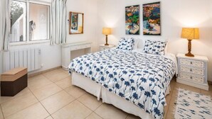 Ein Schlafzimmer mit einem großen Bett, zwei Nachttischen, einem Heizkörper, einem Fenster mit Vorhängen und zwei Bildern an der Wand.