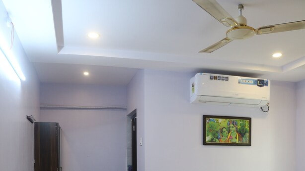 A bedroom with a bed, a ceiling fan, an air conditioner, a wall-mounted painting, and a wooden chair. - SK Guest House  (Visakhapatnam)