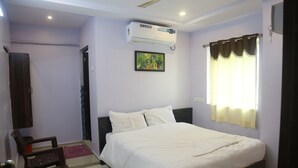 A bedroom with a bed, a chair, a wall-mounted air conditioner, a painting, and a window with curtains. - SK Guest House  (Visakhapatnam)