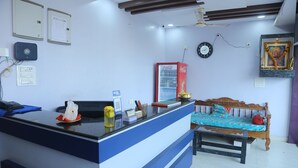 A reception area with a counter, a clock, a refrigerator, and a bed with a blue and red bedspread. - SK Guest House  (Visakhapatnam)