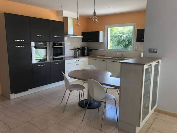 A modern kitchen with dark cabinets, a round dining table, and two white chairs.