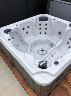 A white hot tub with multiple jets, a control panel, and a drain plug.