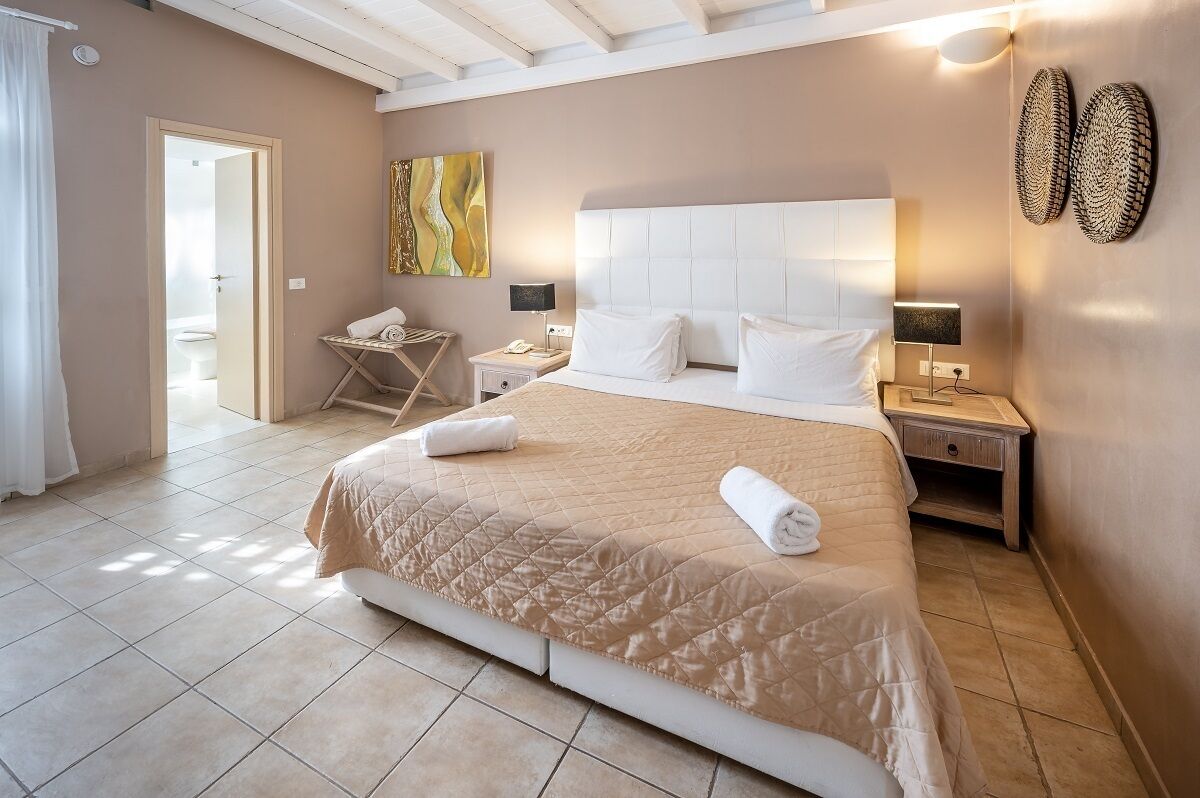 A hotel room with a large bed, two bedside tables, a nightstand, a wall-mounted lamp, and a painting.