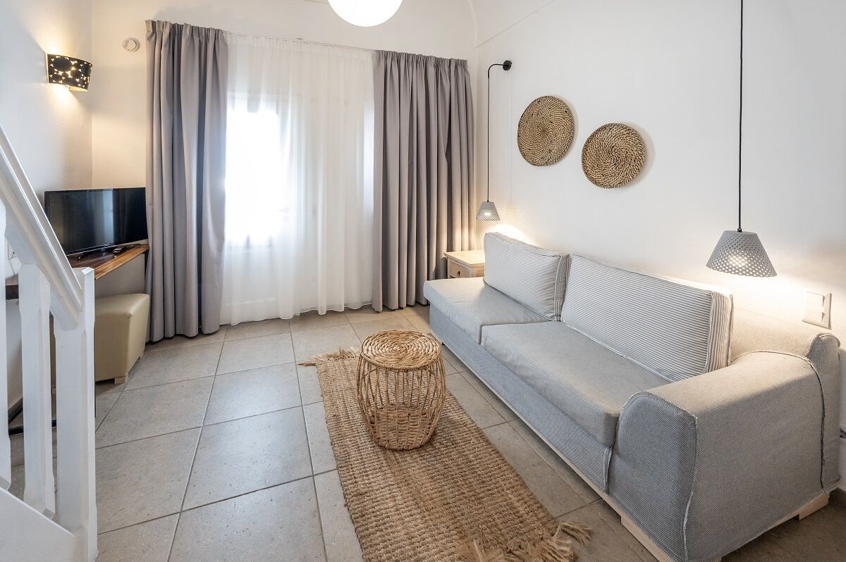 Una sala de estar moderna con un sofá gris, un televisor, una mesa de centro tejida y una escalera.