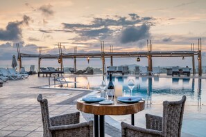 Un espace repas aménagé au bord de la piscine, avec une table pour deux, donnant sur la piscine et les chaises longues.