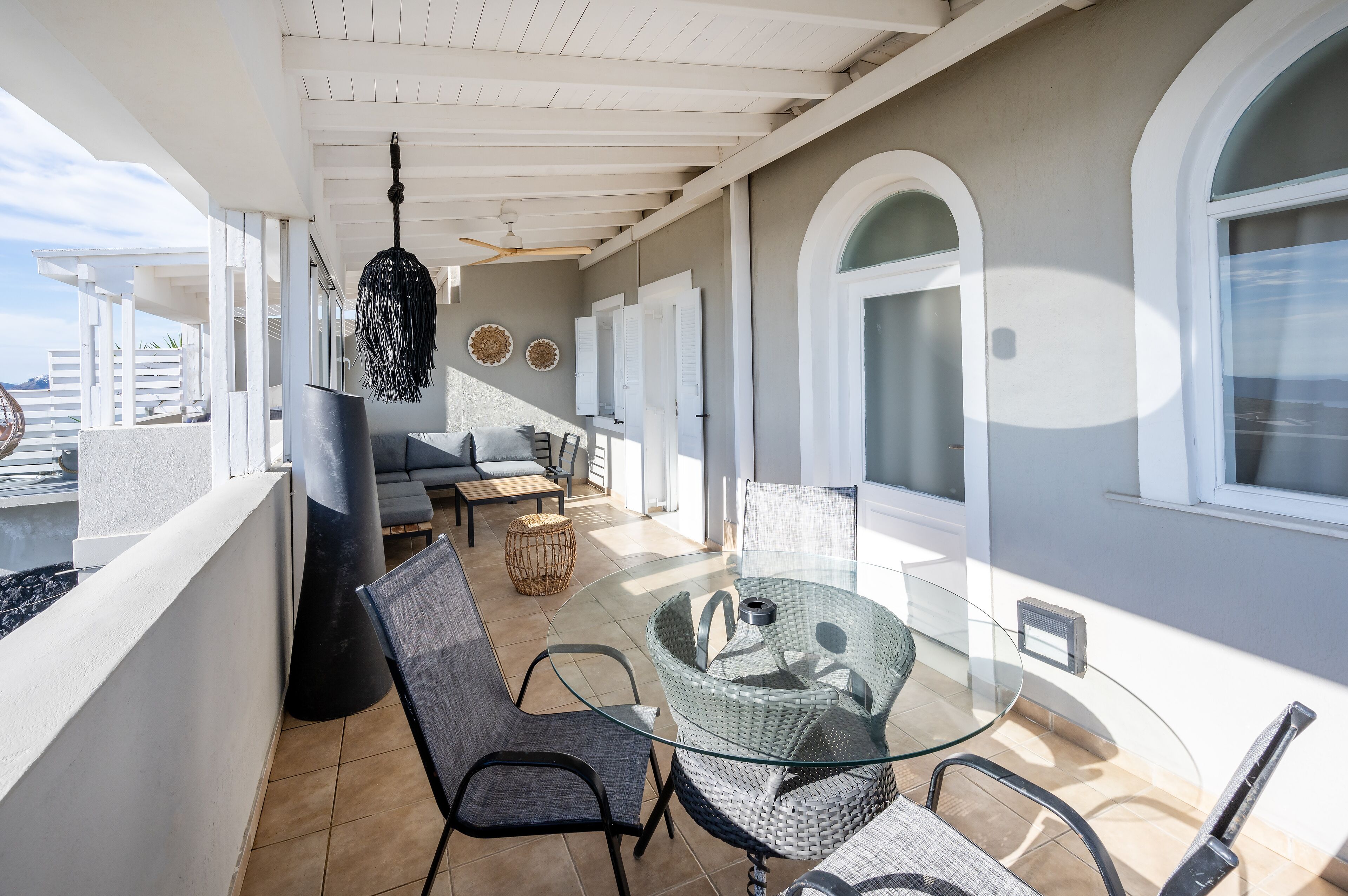 Un balcon avec une table en verre, des chaises en osier et un luminaire suspendu.