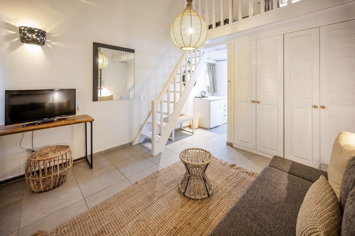 A modern living room with a television, wicker furniture, a staircase, and a wardrobe.
