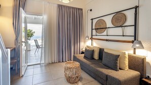 Un salon avec un canapé, un tabouret en osier et une vue sur la mer, visible à travers une porte vitrée.