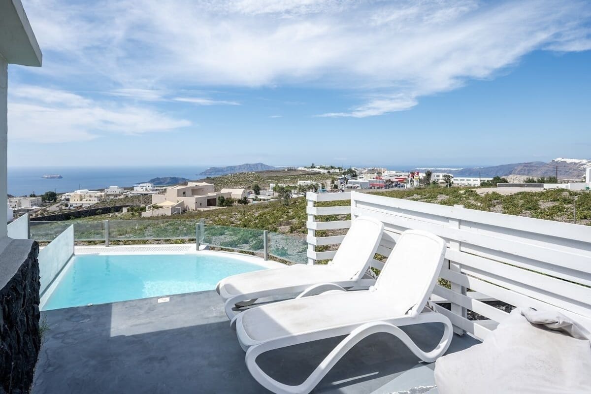 A rooftop pool with white lounge chairs and a view of the sea and distant buildings.