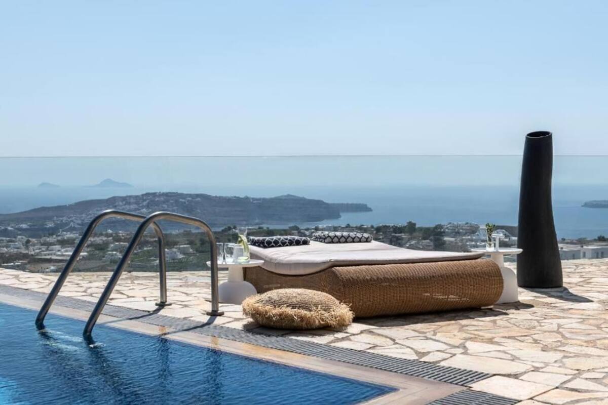 A pool area with a view of the sea and mountains, a lounge chair, and a tall vase.