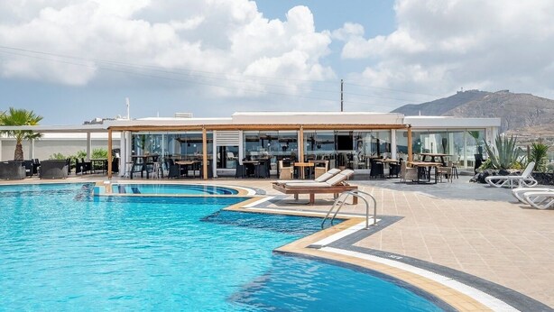 Ein Swimmingpool mit Liegestühlen und Tischen, eine überdachte Sitzecke und eine Bergkulisse.