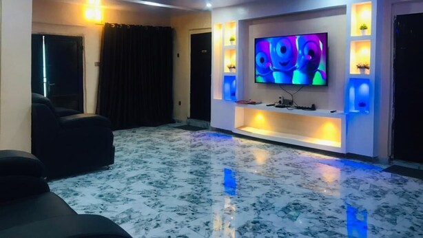 A modern living room with a large flat-screen TV, black leather sofas, a marble floor, and blue LED lighting on the ceiling. - Umbrella Properties Eleyele Ibadan (Ibadan)