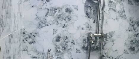 Un baño con pared de diseño de mármol, un lavamanos blanco de pedestal y un cabezal de ducha de mano.