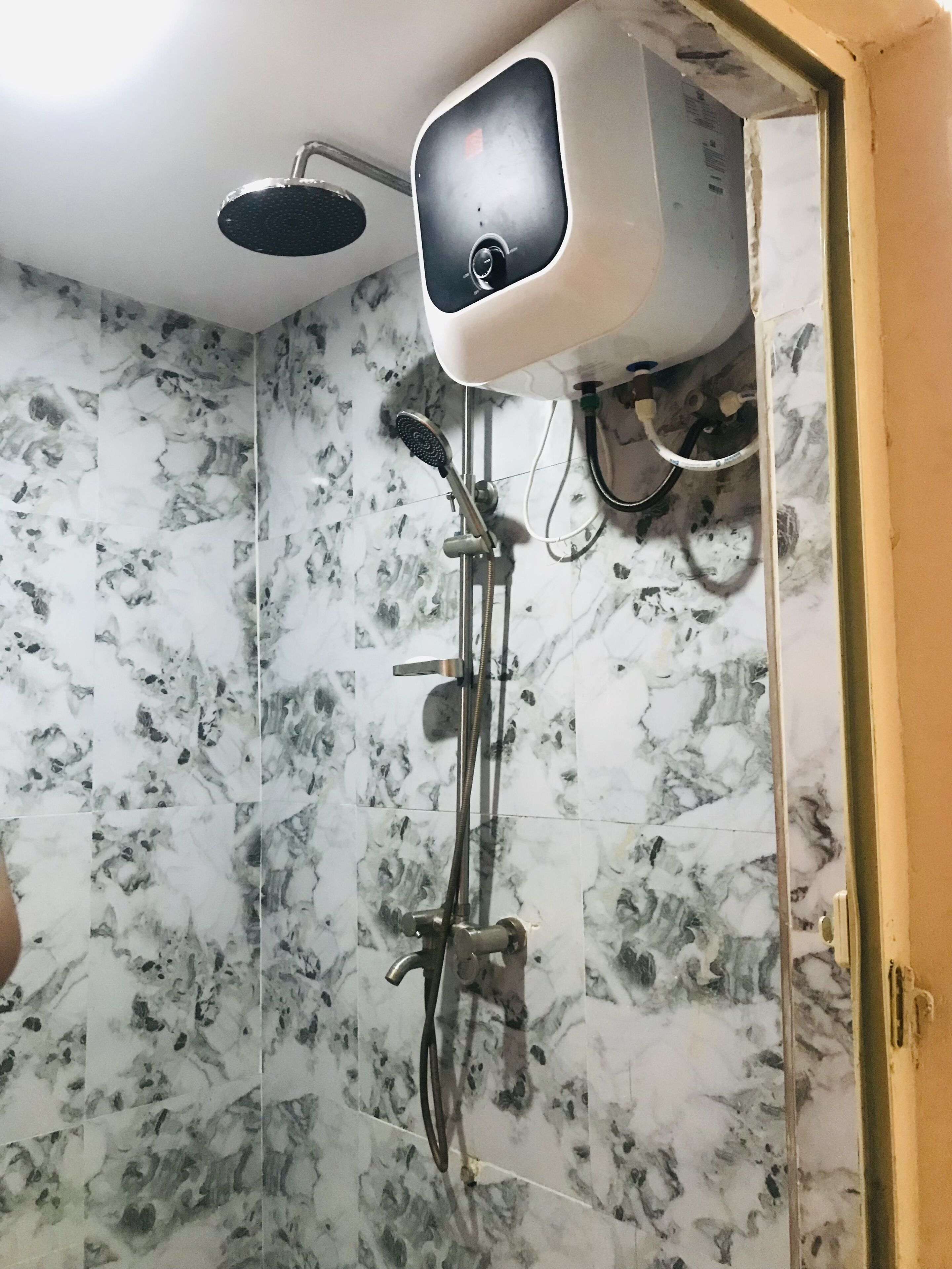 A shower with a handheld showerhead and a fixed overhead showerhead, connected to a wall-mounted control panel.