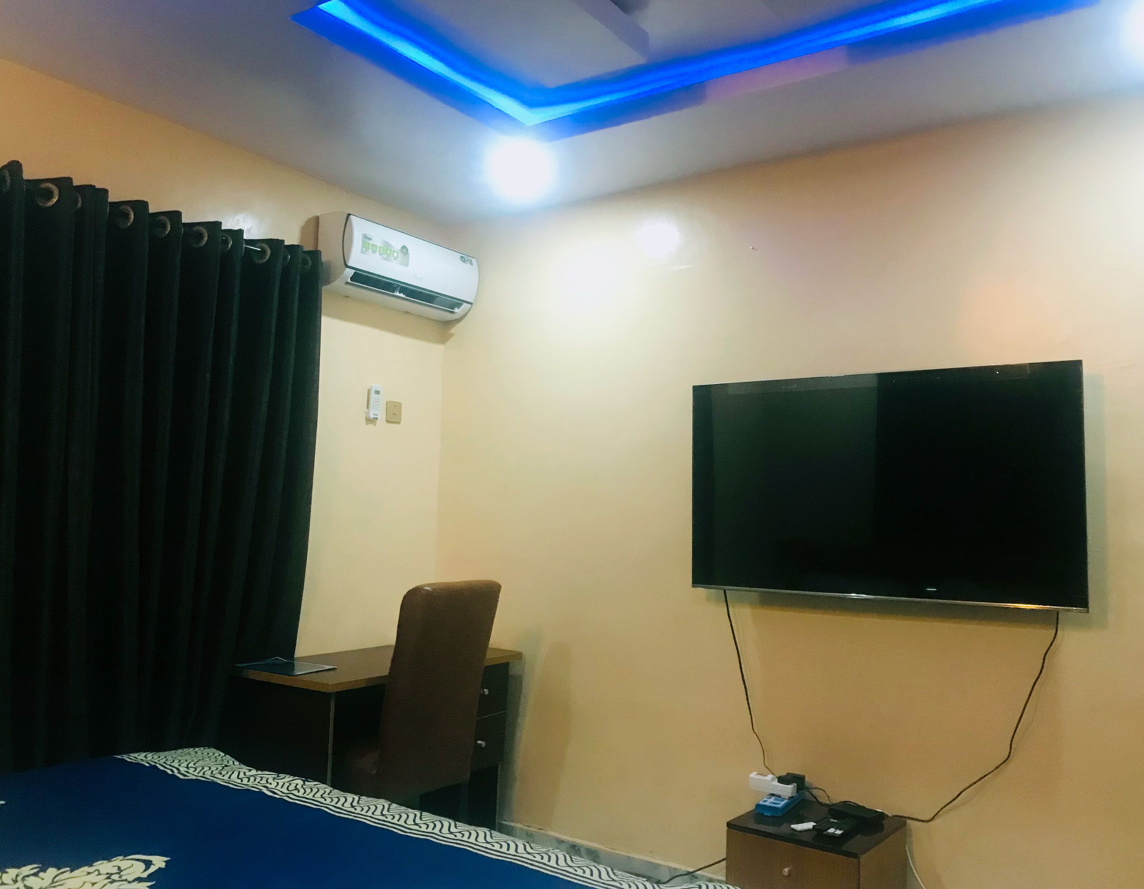 Habitación de hotel con cama, escritorio, silla, televisor de pantalla plana montado en la pared, equipo de aire acondicionado y toma de corriente.