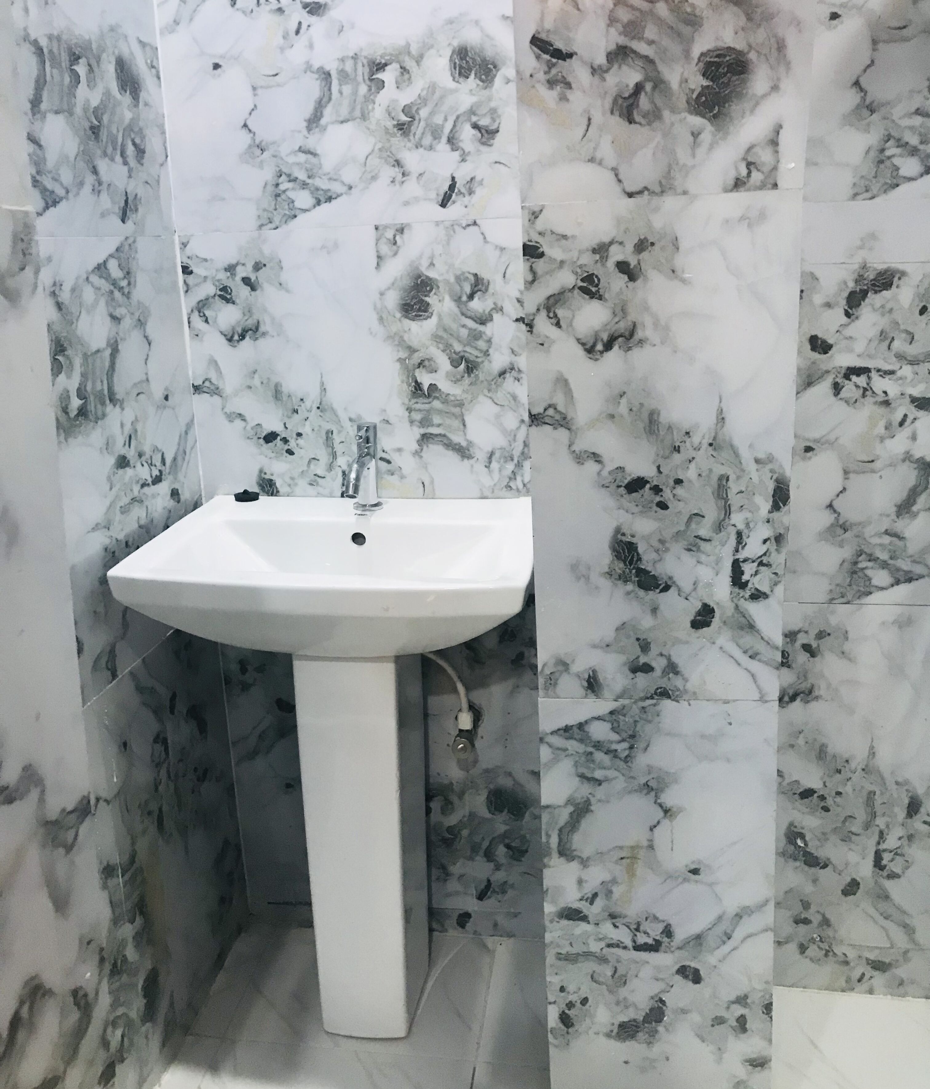 Un baño con un lavamanos blanco sobre pedestal frente a una pared con azulejos tipo mármol.