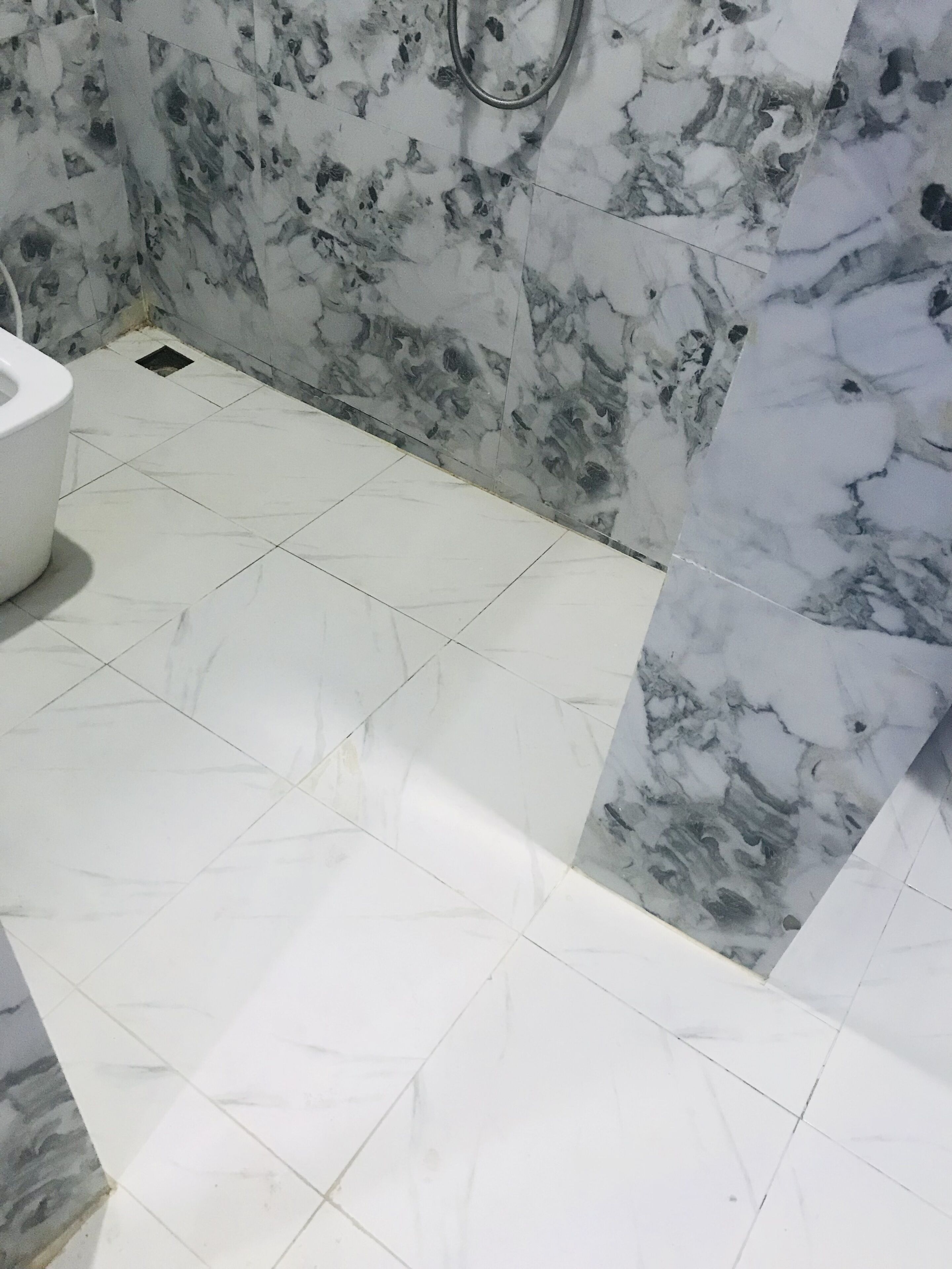 A bathroom with white and marble tiles, a toilet, and a shower area.