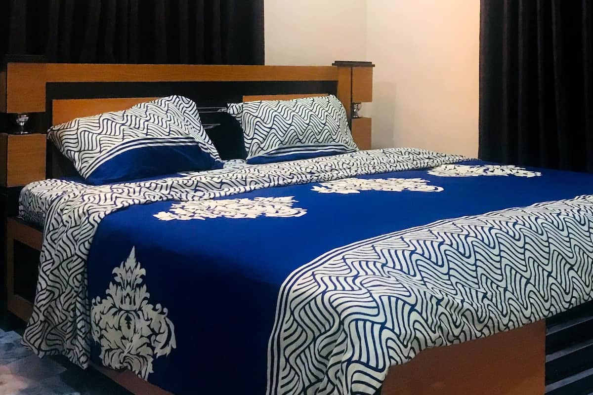 A bed with a patterned bedspread and pillows, a wooden headboard, and a bedside table with a lamp.