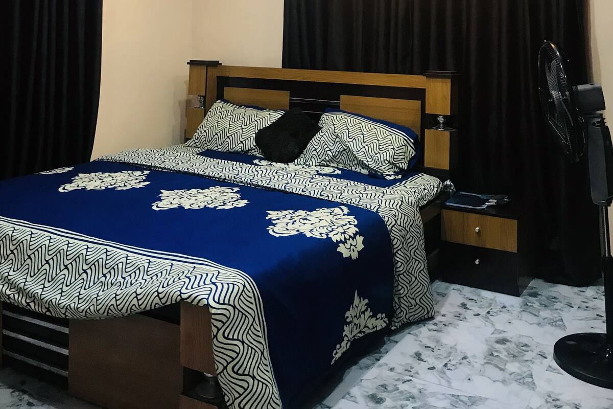 A bedroom with a bed, curtains, a fan, and a nightstand.