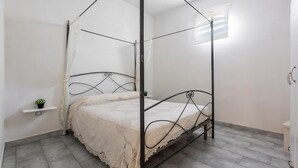 Un lit à baldaquin surmonté d’une couvre-lit en dentelle, une petite plante en pot posée sur une étagère et une fenêtre avec des stores.