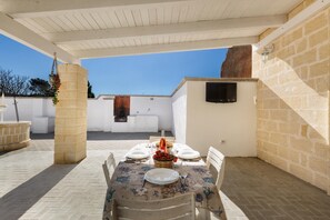 Una terrazza esterna con un tavolo apparecchiato per mangiare, pilastri in pietra e una TV montata a parete.