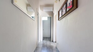 Un couloir étroit au sol carrelé, une porte au fond et un tableau encadré accroché au mur.