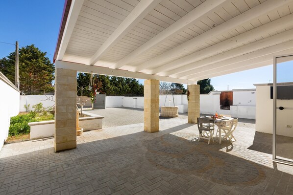 Un patio coperto con pilastri in pietra, un tavolo con sedie e un barbecue.