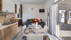 Une cuisine moderne avec des meubles en bois, un four encastré et un évier. Une table à manger avec des chaises est placée devant un canapé gris. Un vase rempli de fleurs se trouve sur la table.