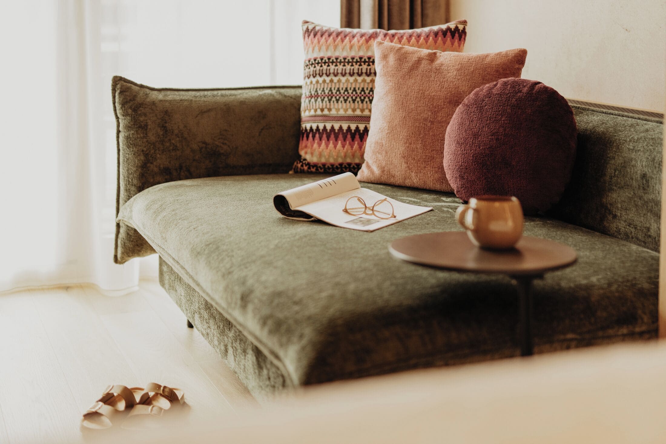 Ein grünes Sofa mit einem Buch, einer Brille und einem Teekännchen auf einem kleinen Tisch.