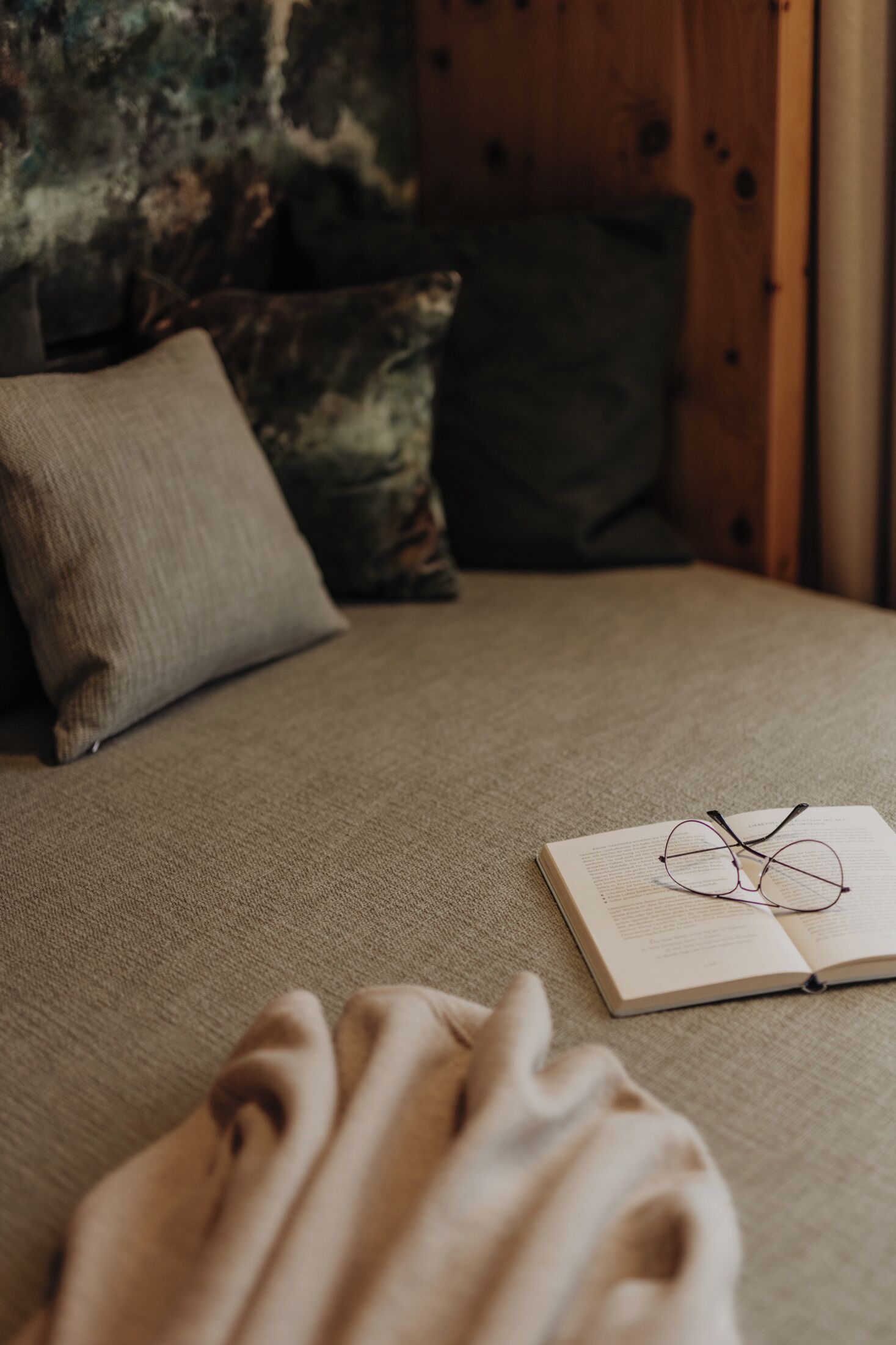 Una cama con un libro, gafas, una manta y almohadas.