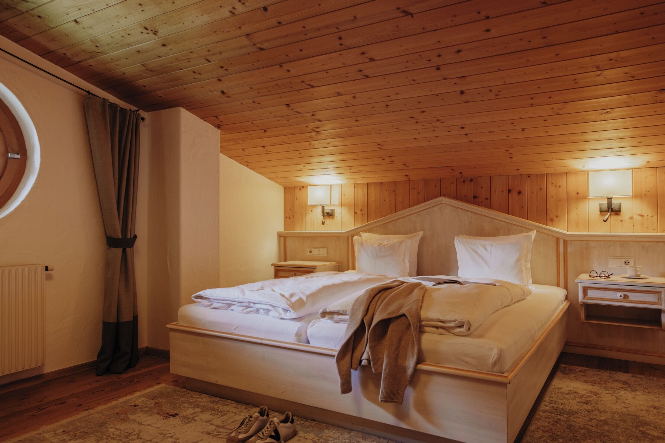 Habitación con paneles de madera, una cama, mesitas de noche y una lámpara de pared.
