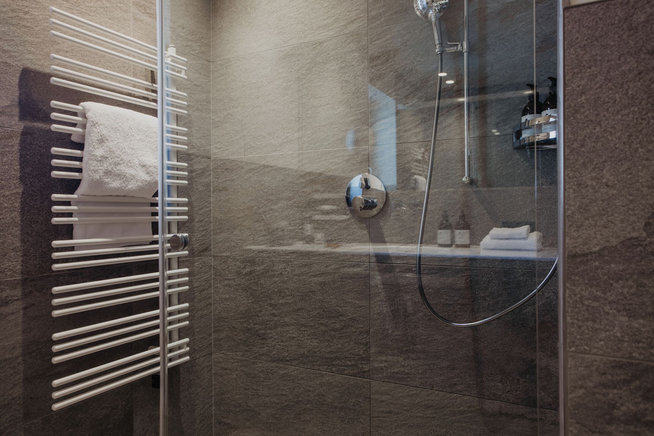 Un baño moderno con cabina de ducha de vidrio, toallero blanco y ducha visible.