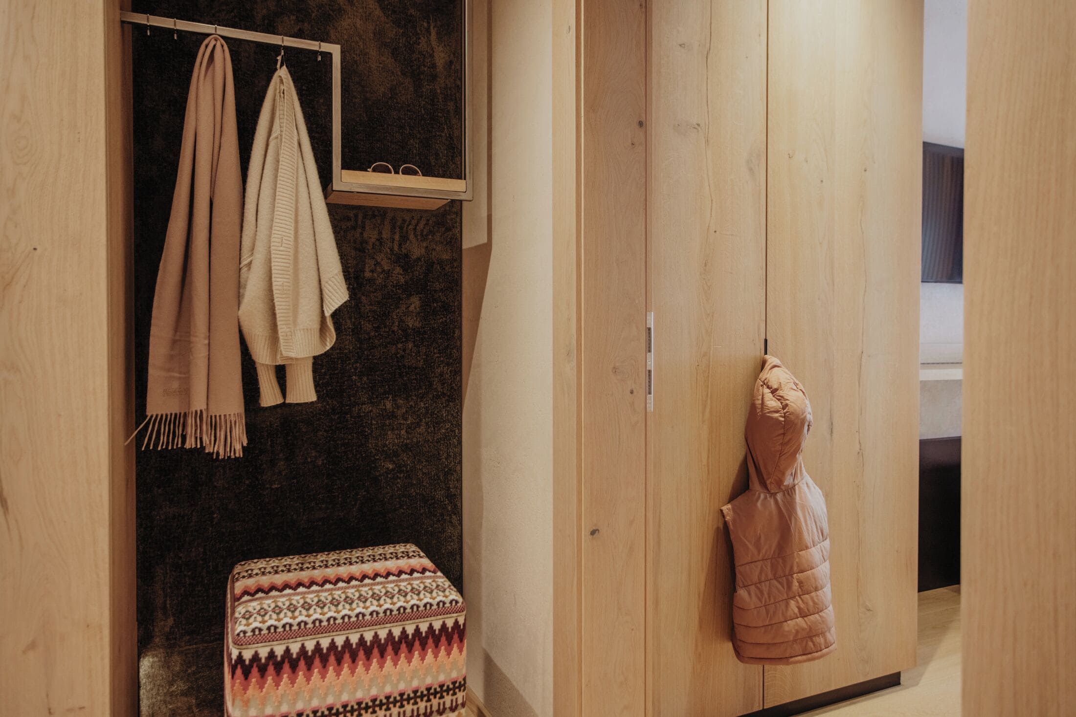A wooden wardrobe with a hanging bag, a bench with patterned cushions, and towels on a rack.