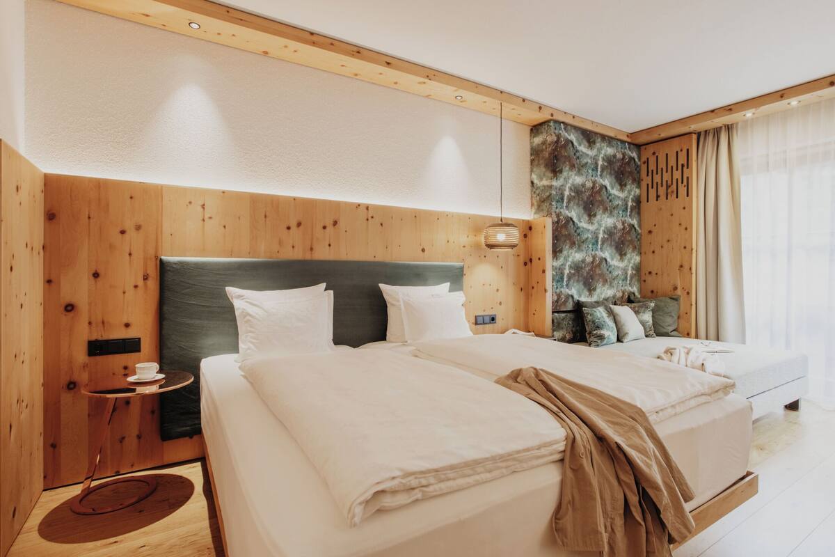 Habitación de hotel con dos camas, paneles de madera, una mesita auxiliar y un detalle decorativo en la pared.