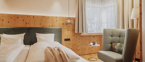 Una habitación de hotel con una cama, una silla, una mesita con una taza y una ventana con cortinas.