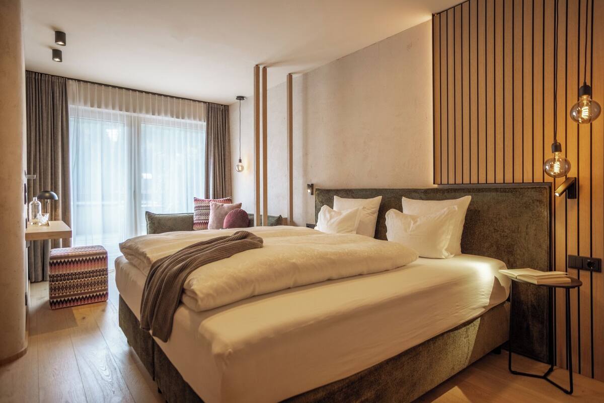 Una habitación de hotel con una cama grande, mesitas de noche, un escritorio y una ventana con cortinas.